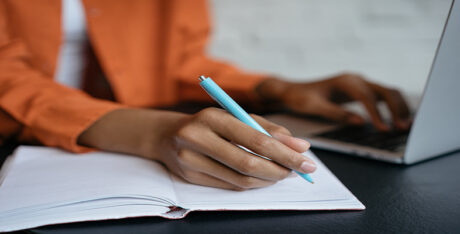 Close-up shot of student hand holding pen and writing in notebook, working at home